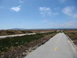 Picture of a bike trail with fields and mountains in the distance.